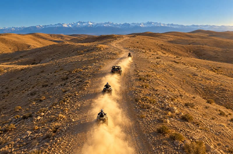 Quads and a buggy in a line on a dusty track, with the snowy Atlas mountains behind